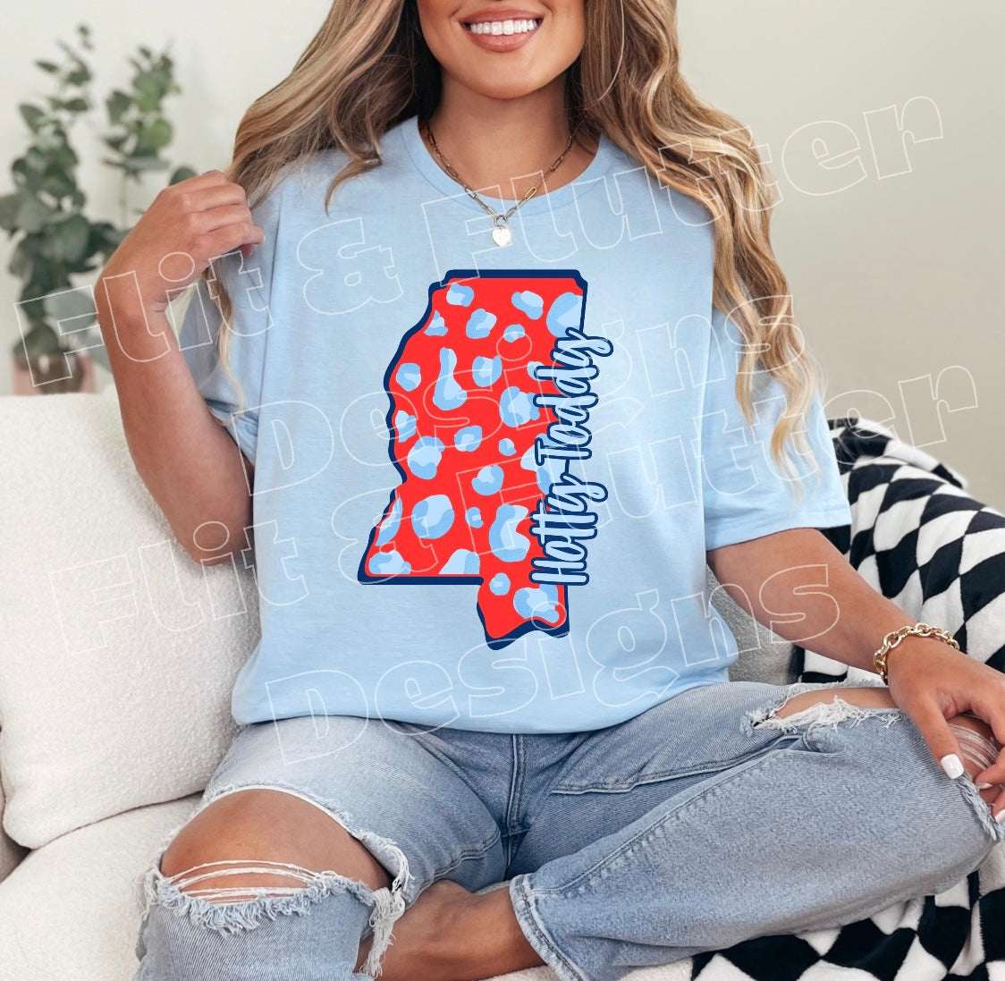 Woman wearing a light blue t-shirt with a colorful design sitting on a couch.