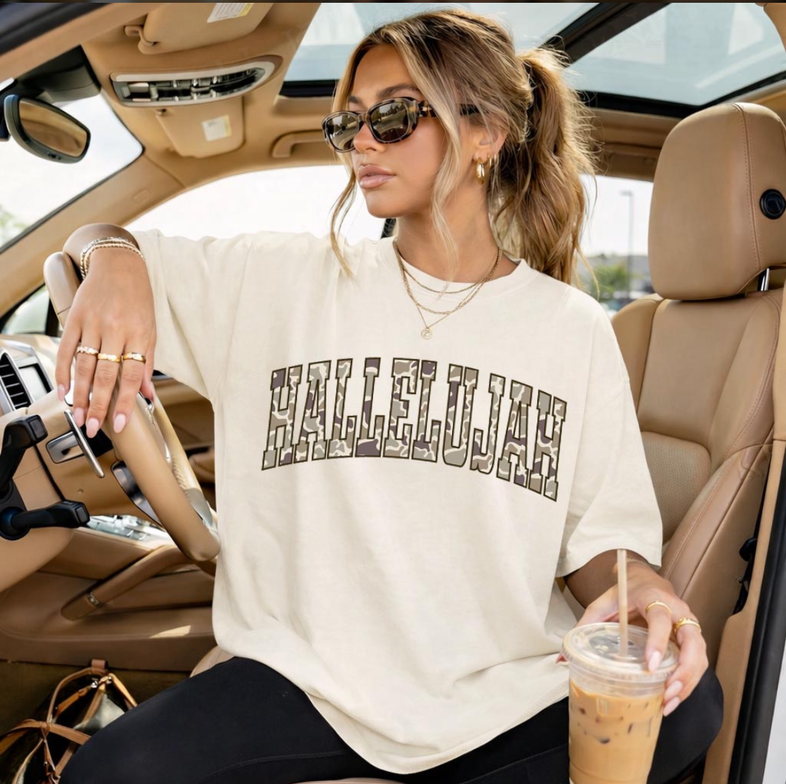 Woman sitting in a car wearing a 'Hallelujah' shirt, holding a drink.