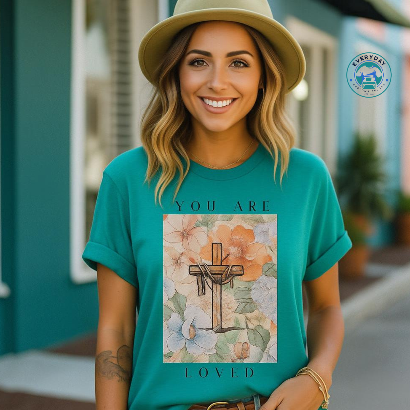 Woman wearing a teal t-shirt with a floral design and text, standing outdoors.