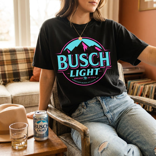 Relaxed person wearing Busch Light Neon Vintage Print Graphic Tee in a cozy setting with warm lighting.