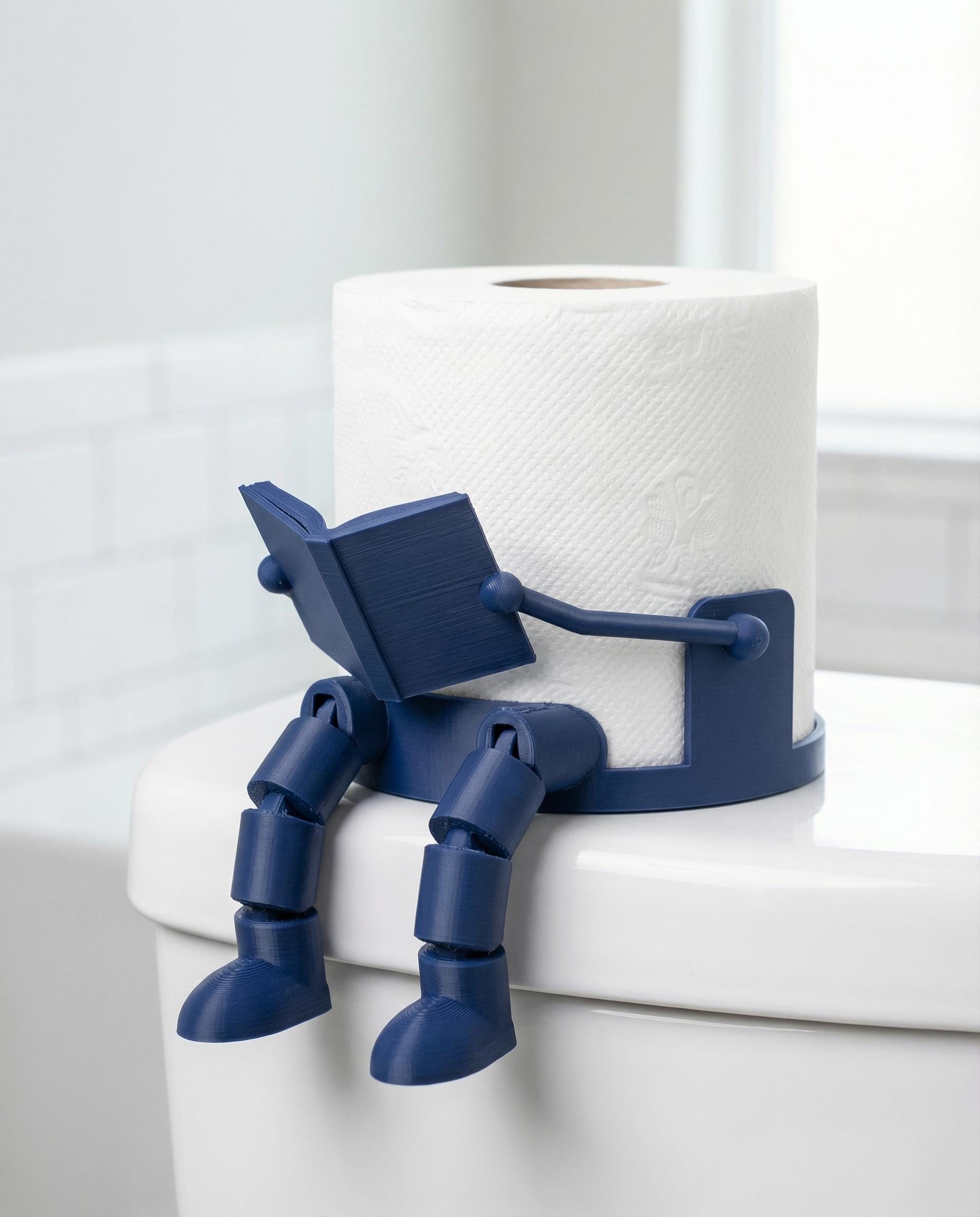 Blue 3D-printed articulated robot reading a book next to a toilet paper roll holder.