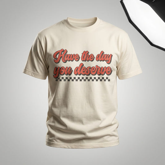 Cream graphic tee with Have The Day You Deserve in red retro script and a checkerboard pattern.