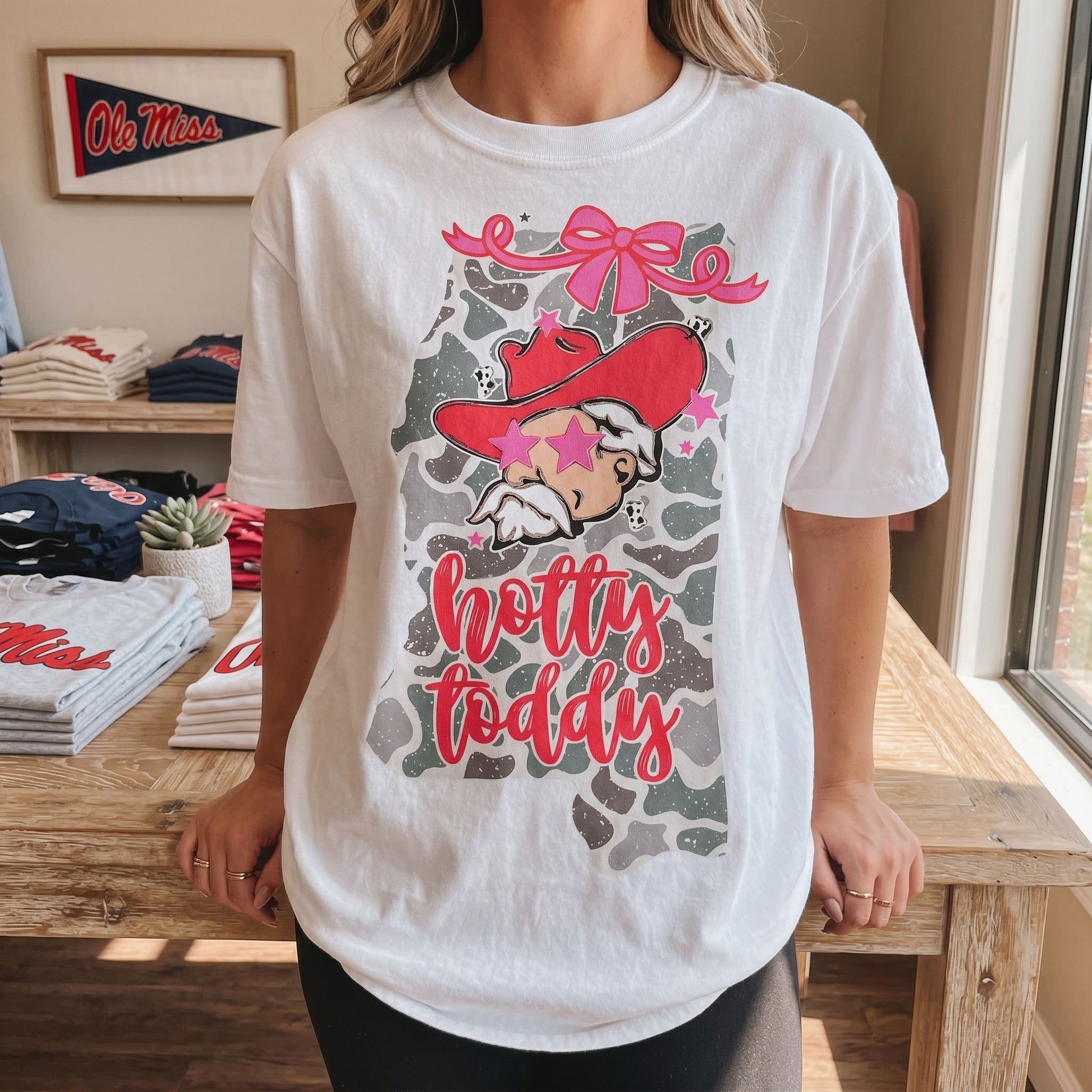 Artistic overhead view of Ole Miss camo mascot t-shirt draped on rustic surface, showcasing print, fabric, and southern boutique style.